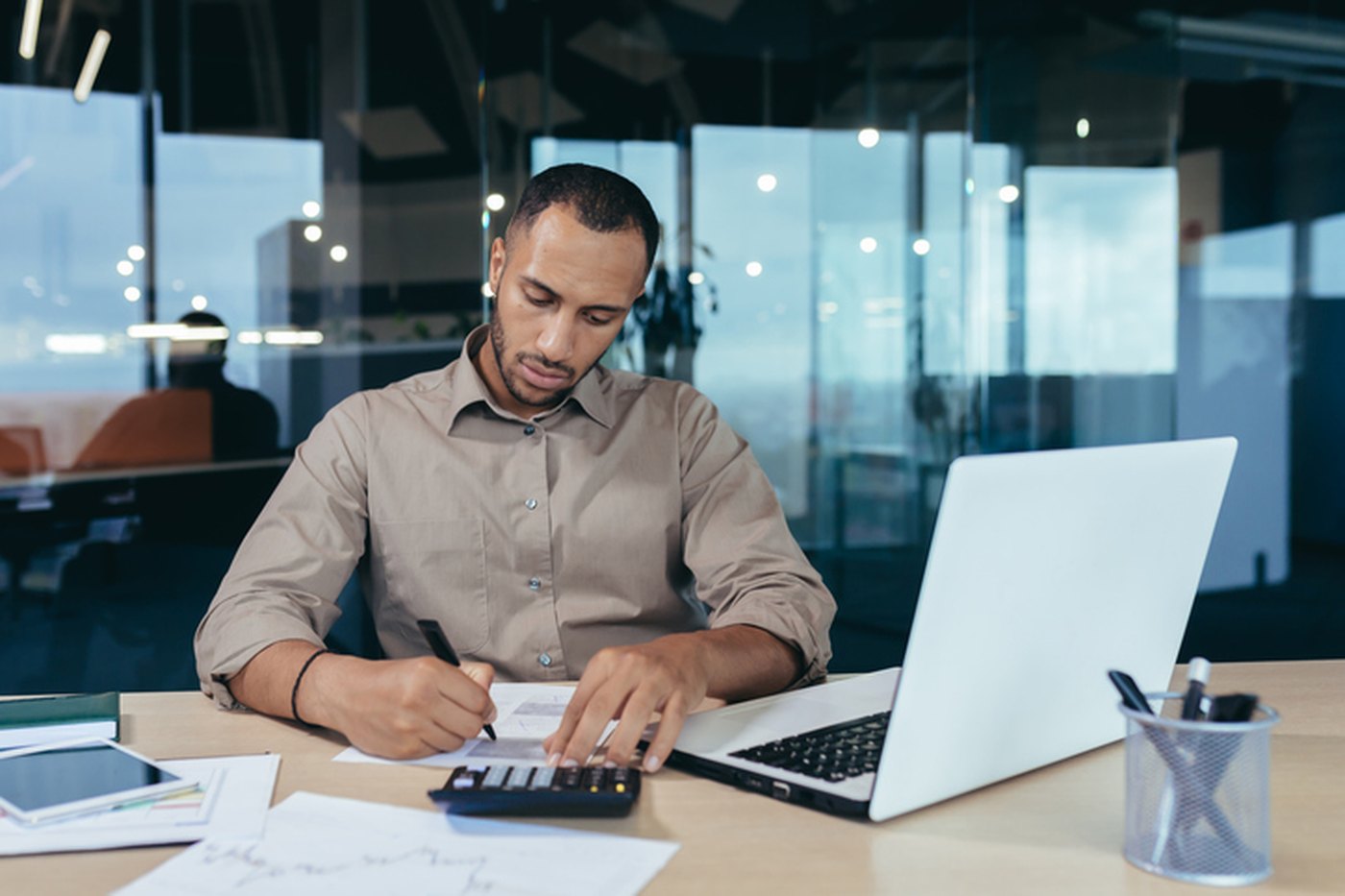 An accountant reconciling accounts with a calculator, ledger, and laptop