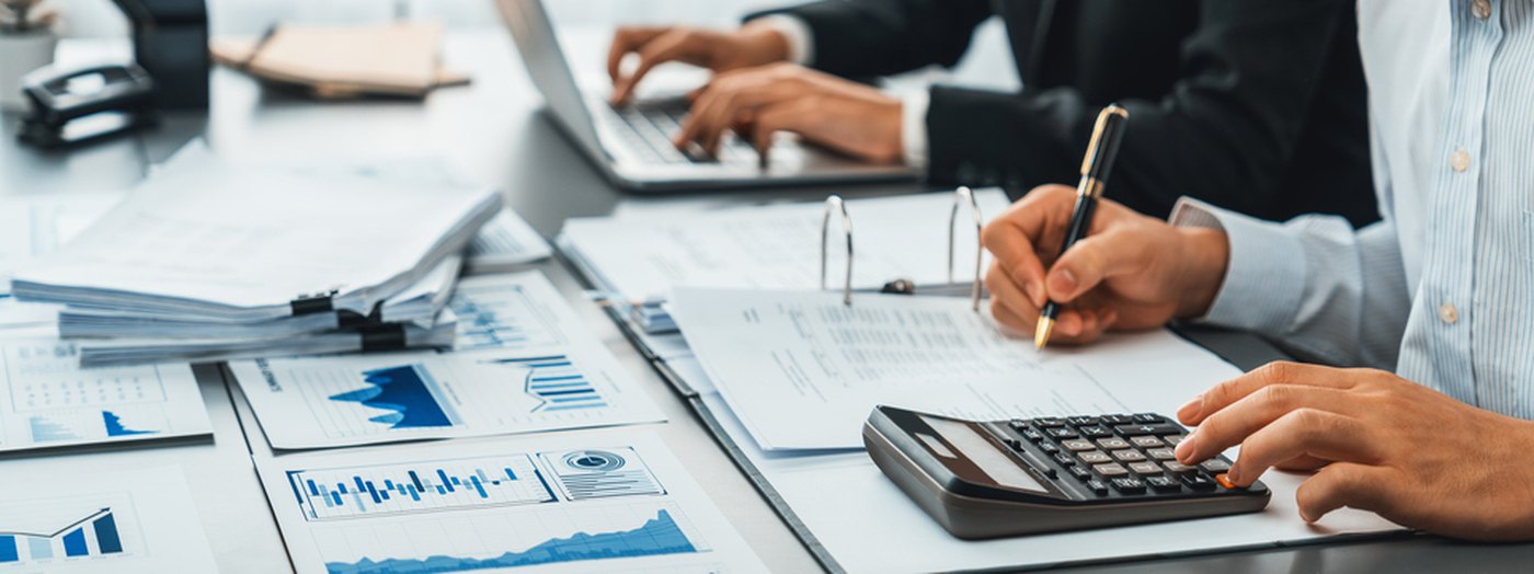 Two analysts reviewing financial charts and running numbers on a calculator