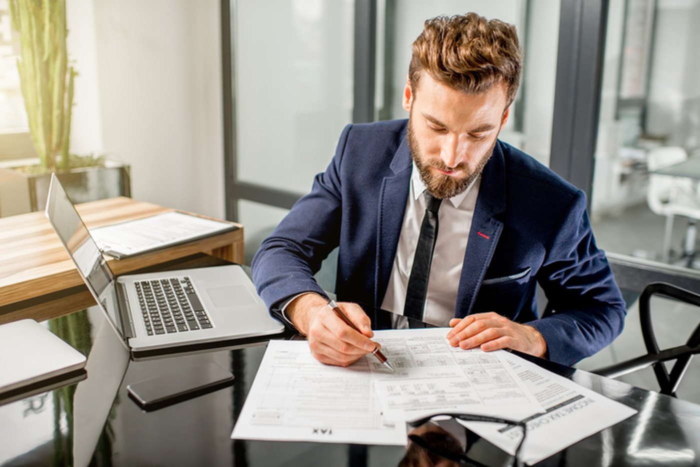 An accountant completing a tax return by hand beside a laptop